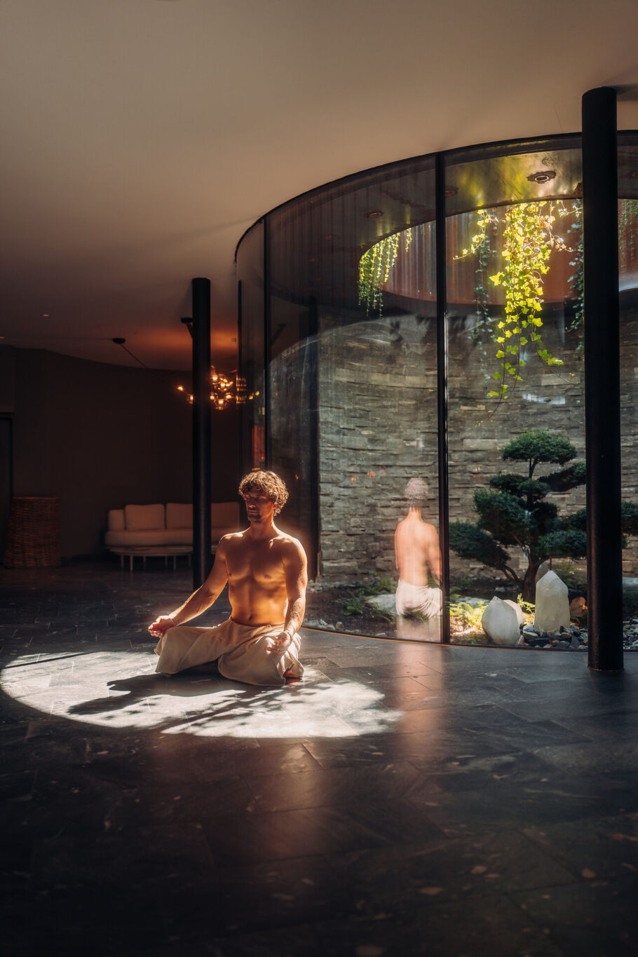 Mann im Schneidersitz im Atrium vor dem Bonsai